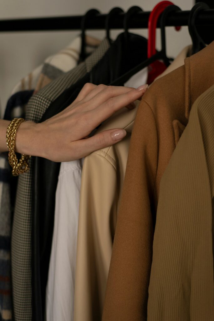 A delicate hand with gold bracelet selecting clothes in a wardrobe, showcasing fashion elegance.